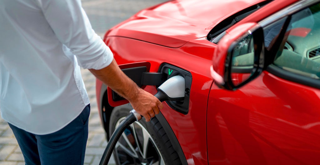 Véhicule électrique en charge sur borne de recharge rapide publique dans un parking français, câble connecté et voyant actif visible